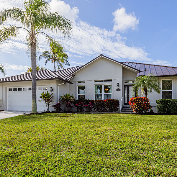 Singlestory white house with a twocar garage front lawn and palm trees on a sunny day Single-story white house with a two-car garage, front lawn, and palm trees on a sunny day.
