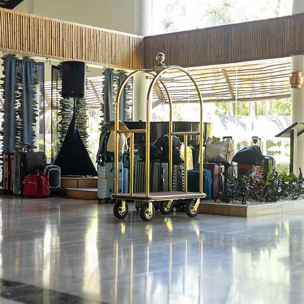 Hotel luggage cart with suitcases and bags in a spacious lobby area near a glass wall and plants Hotel luggage cart with suitcases and bags in a spacious lobby area near a glass wall and plants.
