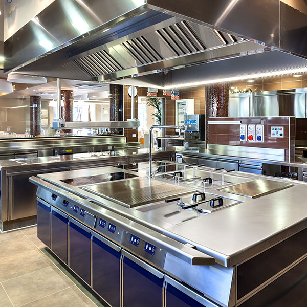 Commercial stainless steel kitchen with a central island stove, range hoods, and sinks, in a busy restaurant setting.